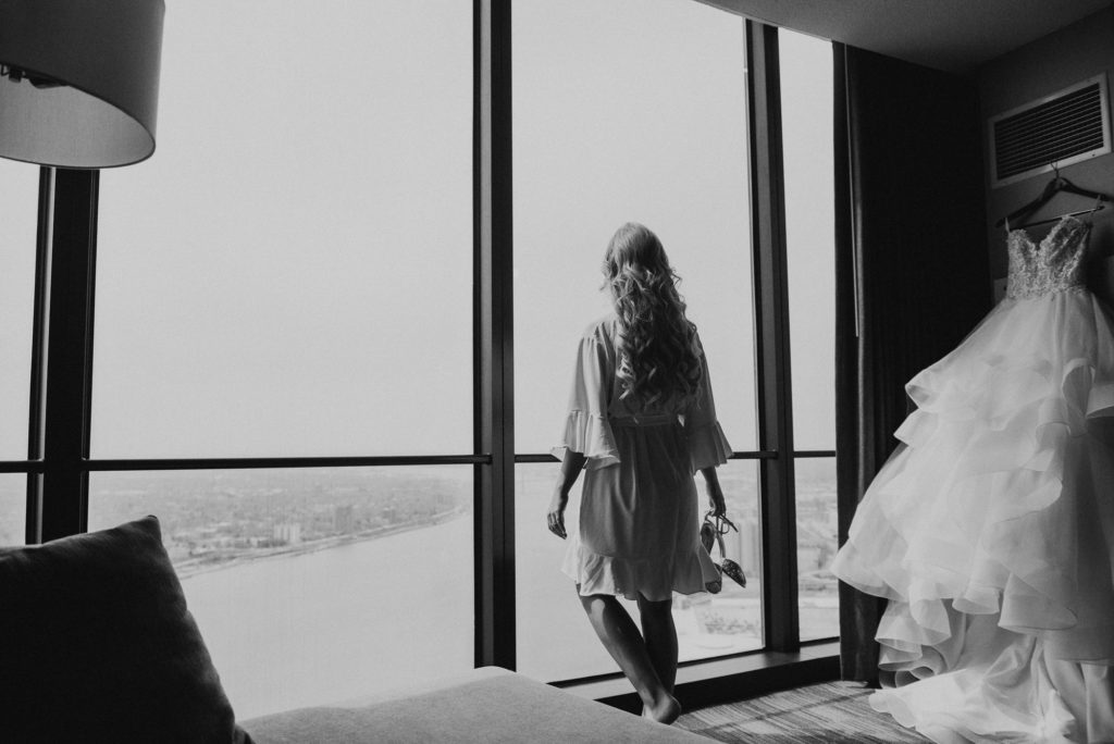 woman looks out the window next to a wedding dress
