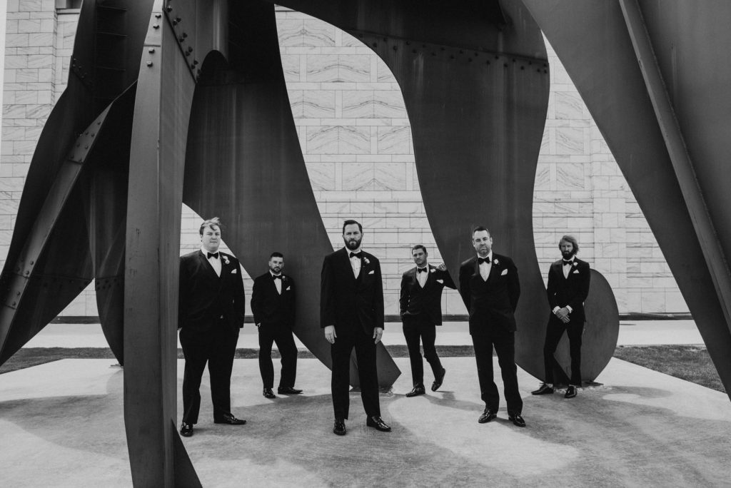 Groom and groomsmen pose under a large art structure