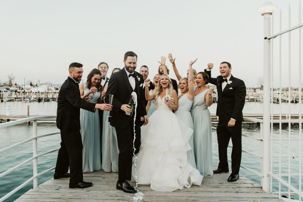 Bridal party laughs as groom shakes up champagne to pop the cork