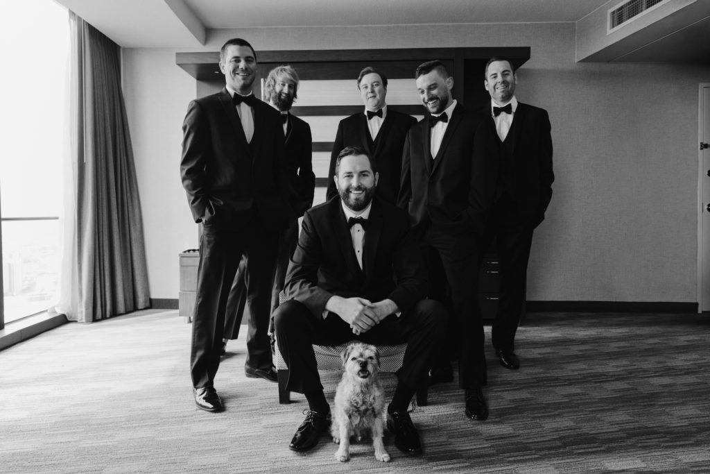 Groom and groomsmen smiling with a dog sitting in front of them